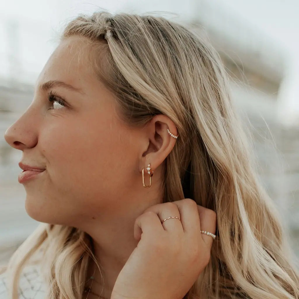 Woman wearing gold hoop earrings and a ring, with a blurred natural background