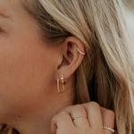 Close-up of a person wearing gold hoop earrings and a ring with pearl accents.