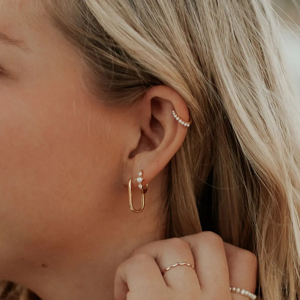 Close-up of a person wearing gold hoop earrings and a ring.