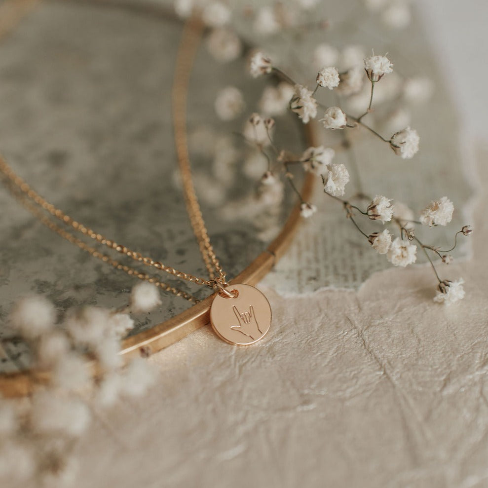 Gold necklace with a round pendant on a textured surface with small white flowers.