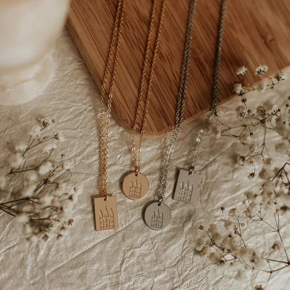 Three gold necklaces with engraved pendants on a textured surface with dried flowers.