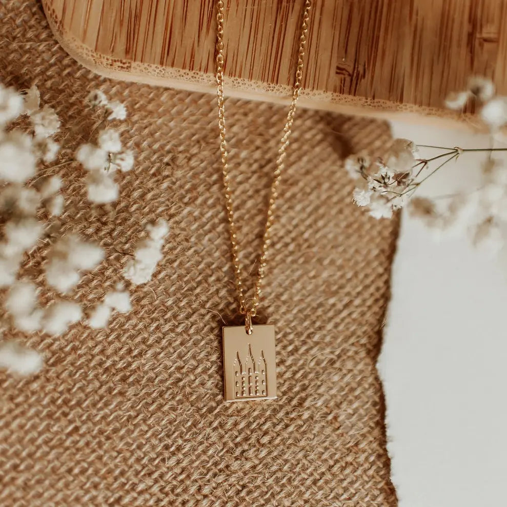 Gold necklace with a pendant on a textured surface with white flowers.