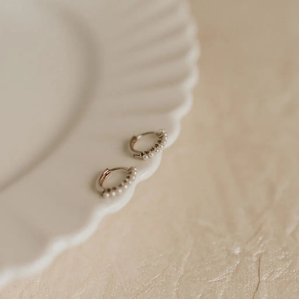Small pearl hoop earrings with pearls on a beige surface