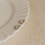 Small pearl hoop earrings with pearls on a beige surface