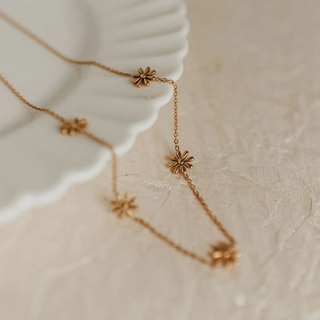 Gold necklace with flower-shaped pendants on a textured beige surface