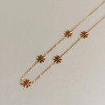 Gold necklace with flower-shaped pendants on a light gray background