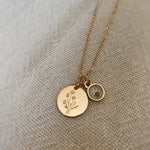Gold necklace with two round pendants on a textured beige background