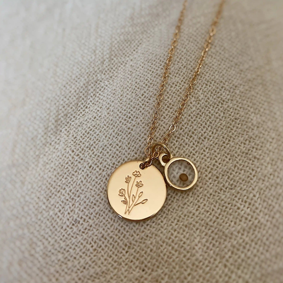 Gold necklace with two round pendants on a textured beige background