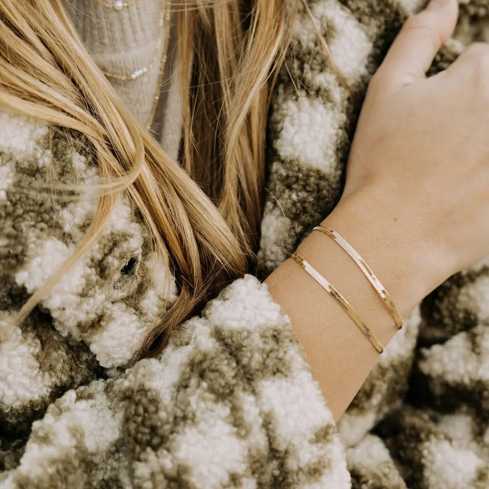 Close-up of a person wearing gold bracelets on a textured surface
