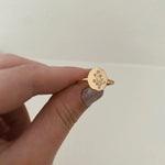 Gold ring with floral engraving held by a hand against a plain background