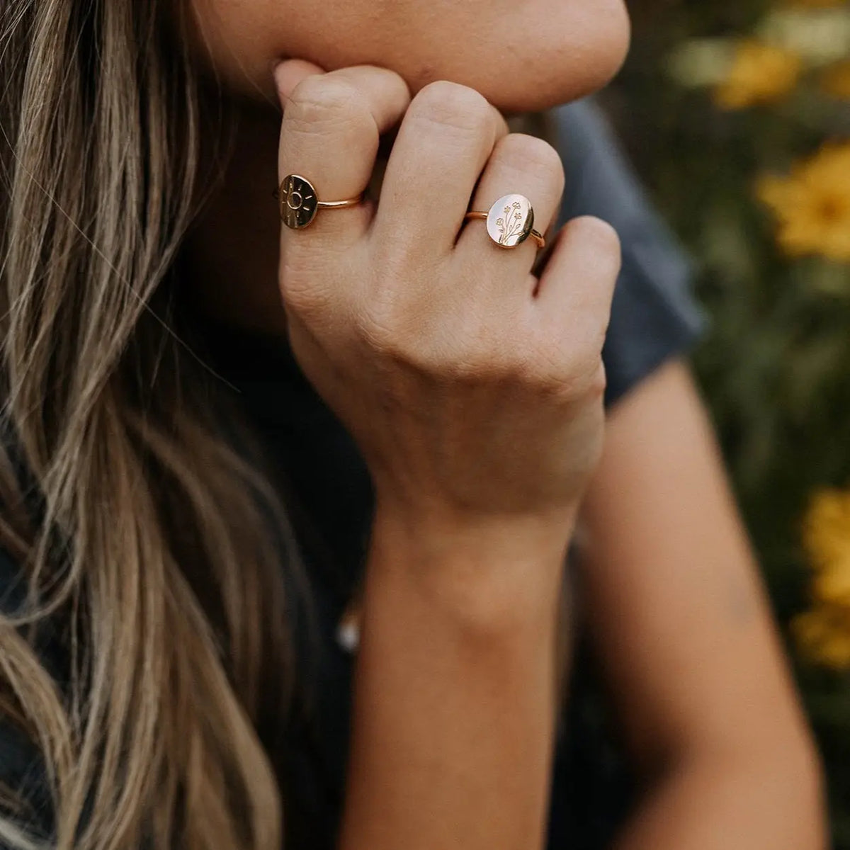 Close-up of a person's hand wearing two rings with a blurred natural background