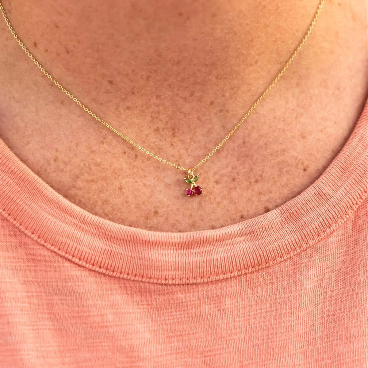 Gold necklace with a small pendant on a person wearing a pink shirt.