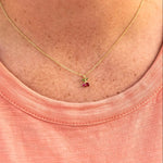 Gold necklace with a small pendant on a person wearing a pink shirt.