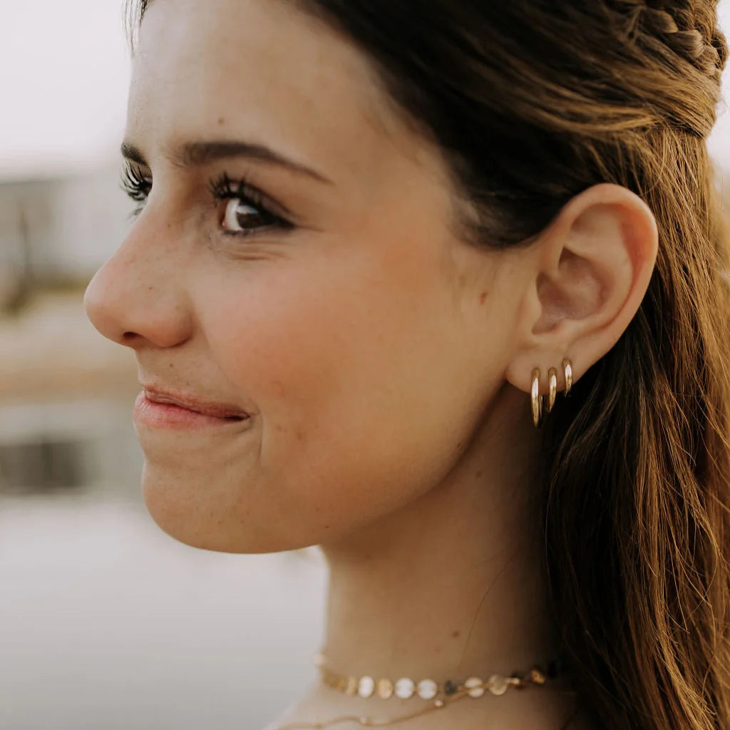 Close-up of a woman wearing gold earrings and a necklace with a blurred background