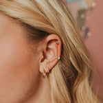 Close-up of an ear with multiple gold earrings against a blurred background