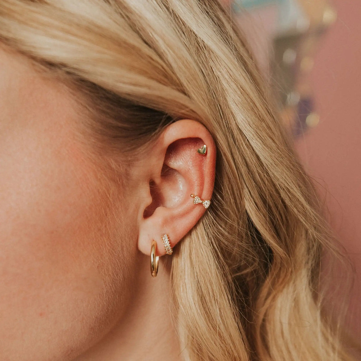 Close-up of an ear with multiple gold earrings against a blurred background