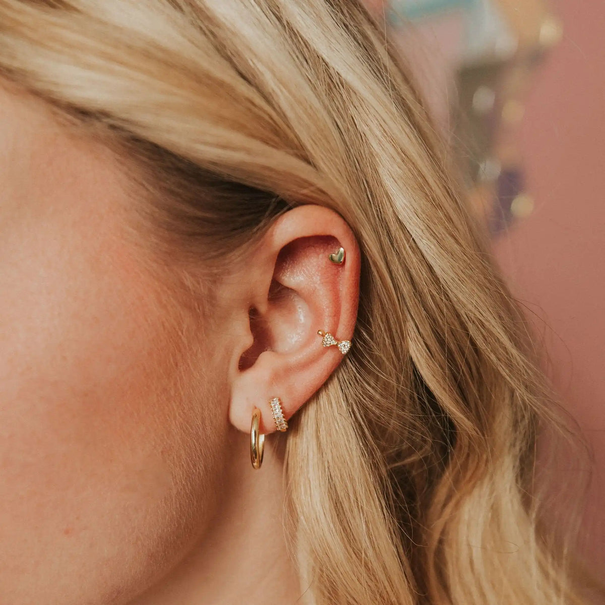 Close-up of a person's ear with gold hoop earrings against a blurred background