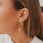 Close-up of a person wearing gold earrings with heart and pearl designs.