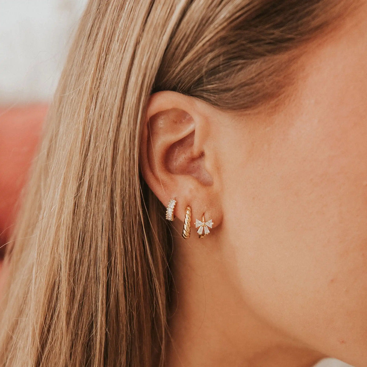 Close-up of an ear wearing gold hoop earrings with small diamonds.
