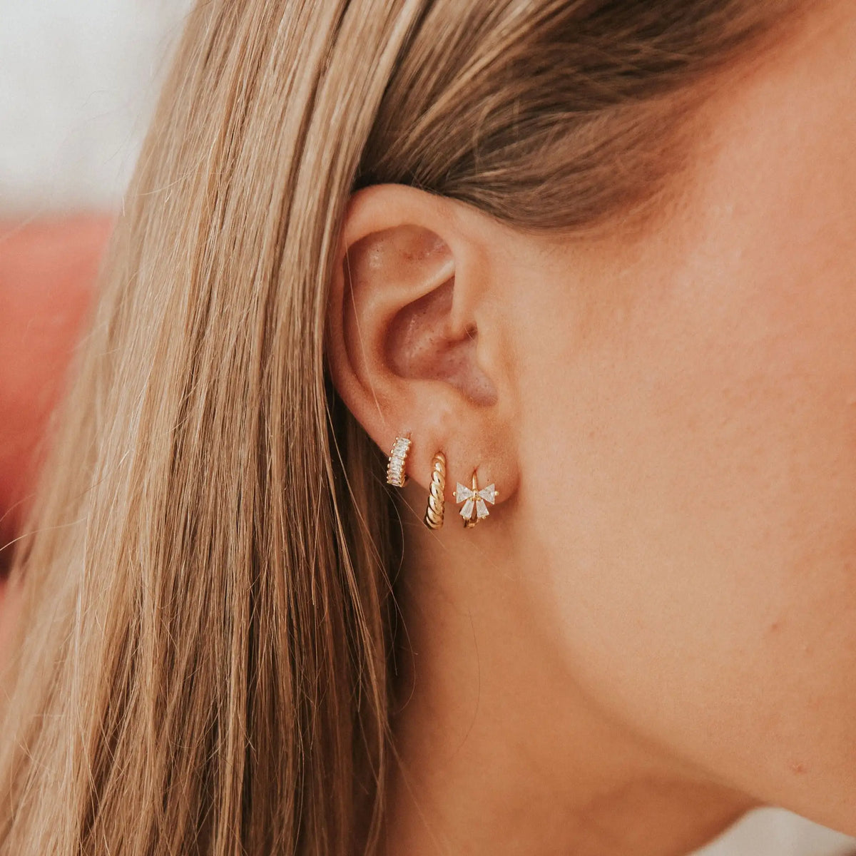 Close-up of an ear wearing gold and diamond earrings with a blurred background