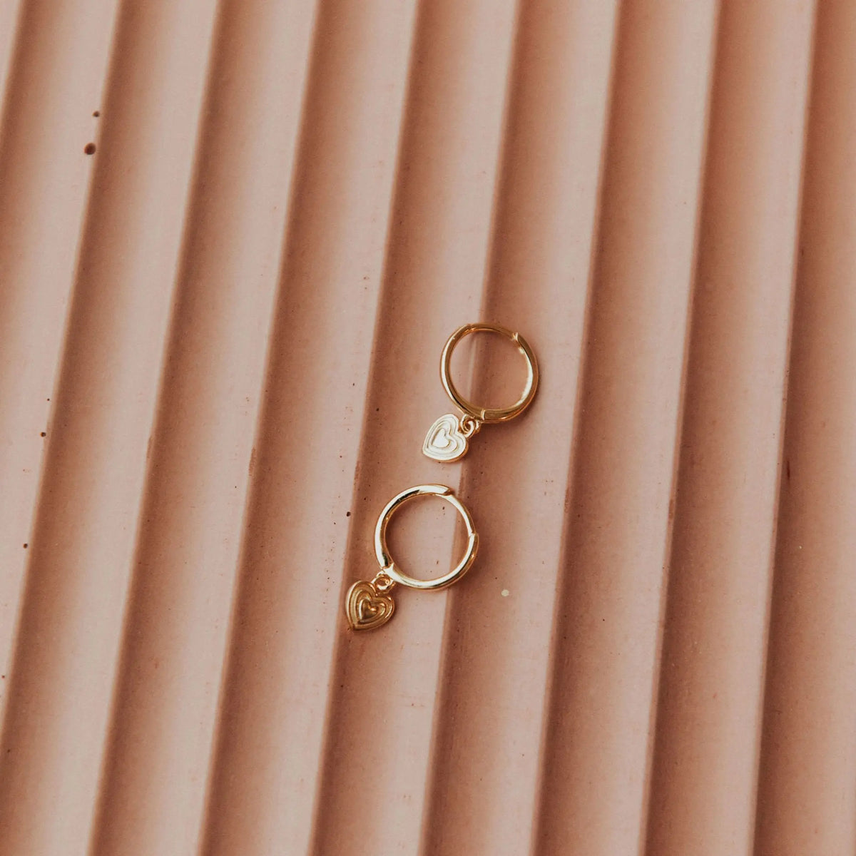 Gold hoop earrings with heart charms on a textured brown surface