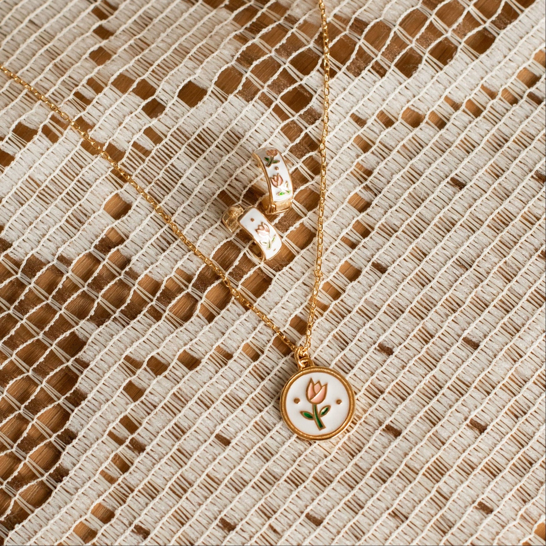 Gold necklace with a tulip floral pendant on a textured beige fabric background