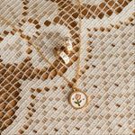 Load image into Gallery viewer, Gold necklace with a tulip floral pendant on a textured beige fabric background
