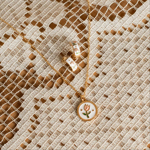 Gold necklace with a tulip floral pendant on a textured beige fabric background