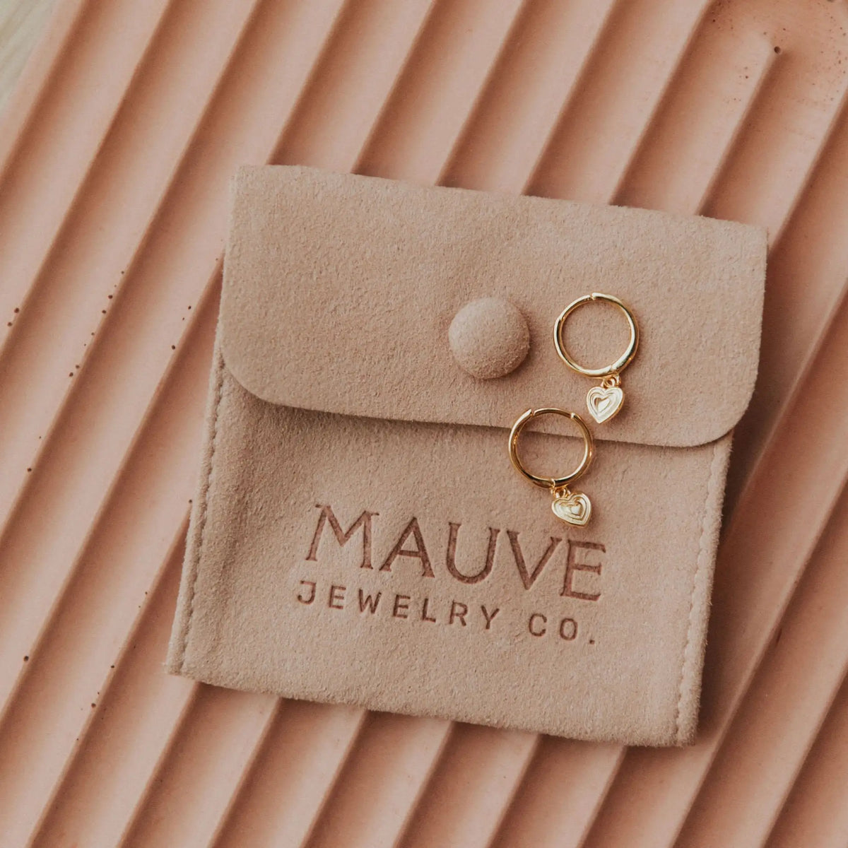 Beige jewelry pouch with 'MAUVE JEWELRY CO.' branding, containing gold earrings on a matching background.