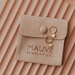 Beige jewelry pouch with 'MAUVE JEWELRY CO.' branding, containing gold earrings on a matching background.