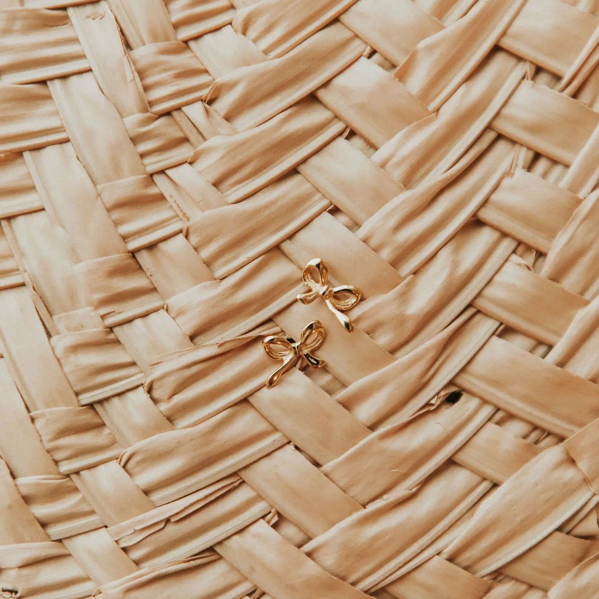 Gold bow-shaped earrings on a woven beige surface