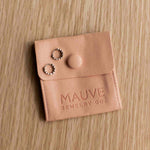Leather jewelry pouch with earrings on a wooden surface, branded 'Mauve Jewelry Co'.
