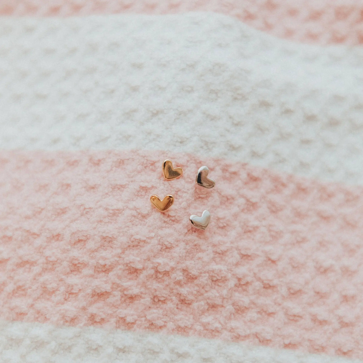 Heart-shaped earrings on a textured pink and white fabric background