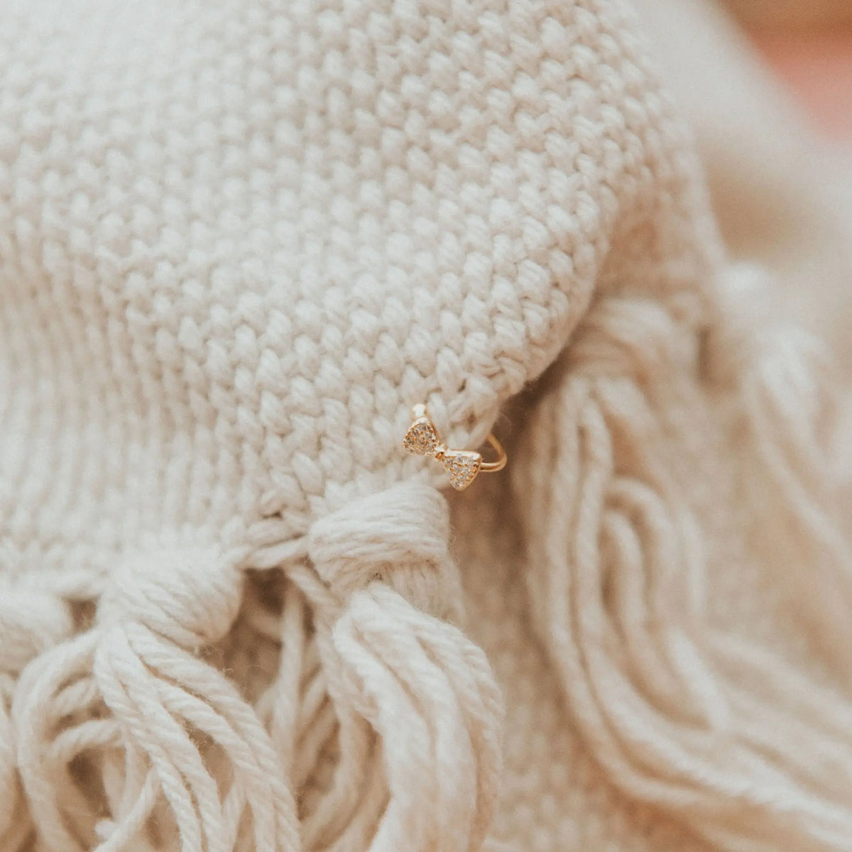 Close-up of beige knitted fabric with a gold earring on a blurred background