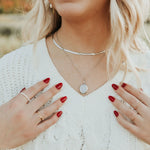 Woman wearing a white sweater with gold necklaces and rings, outdoors.