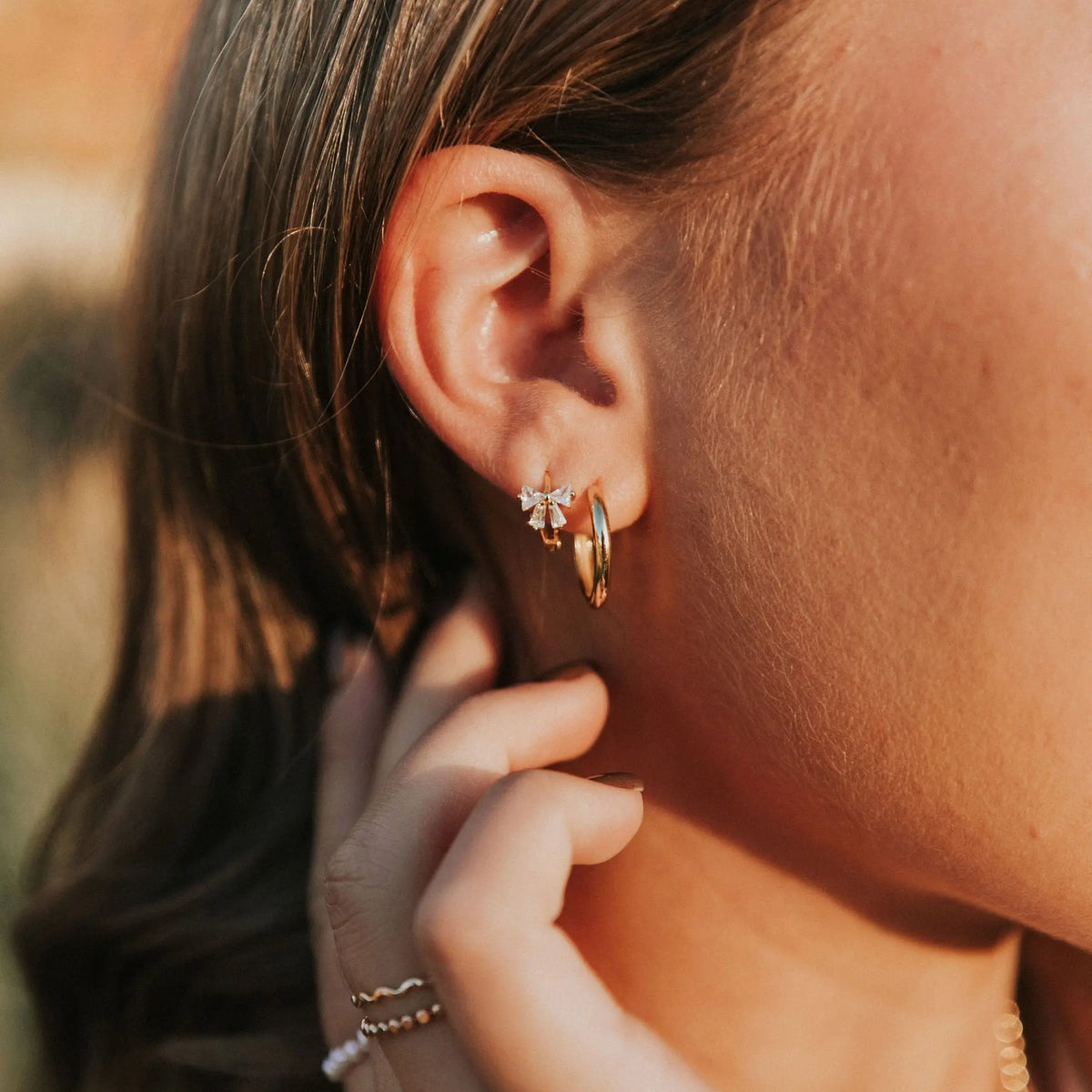 Close-up of an ear with gold hoop earrings and a blurred background