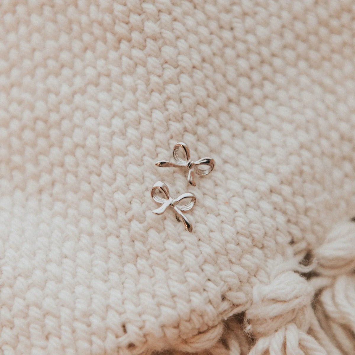 Pair of gold bow-shaped earrings on a textured beige fabric background
