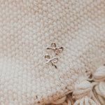 Pair of gold bow-shaped earrings on a textured beige fabric background