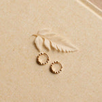 Gold hoop earrings on a textured beige surface with a leaf