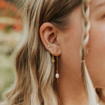 Close-up of a person wearing gold earrings with pearl drops, blurred background