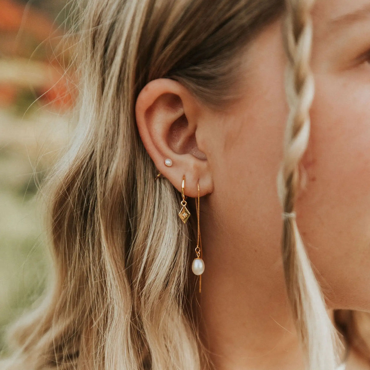 Close-up of a woman's ear wearing gold earrings with pearls.