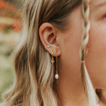 Close-up of a woman's ear wearing gold earrings with pearls.