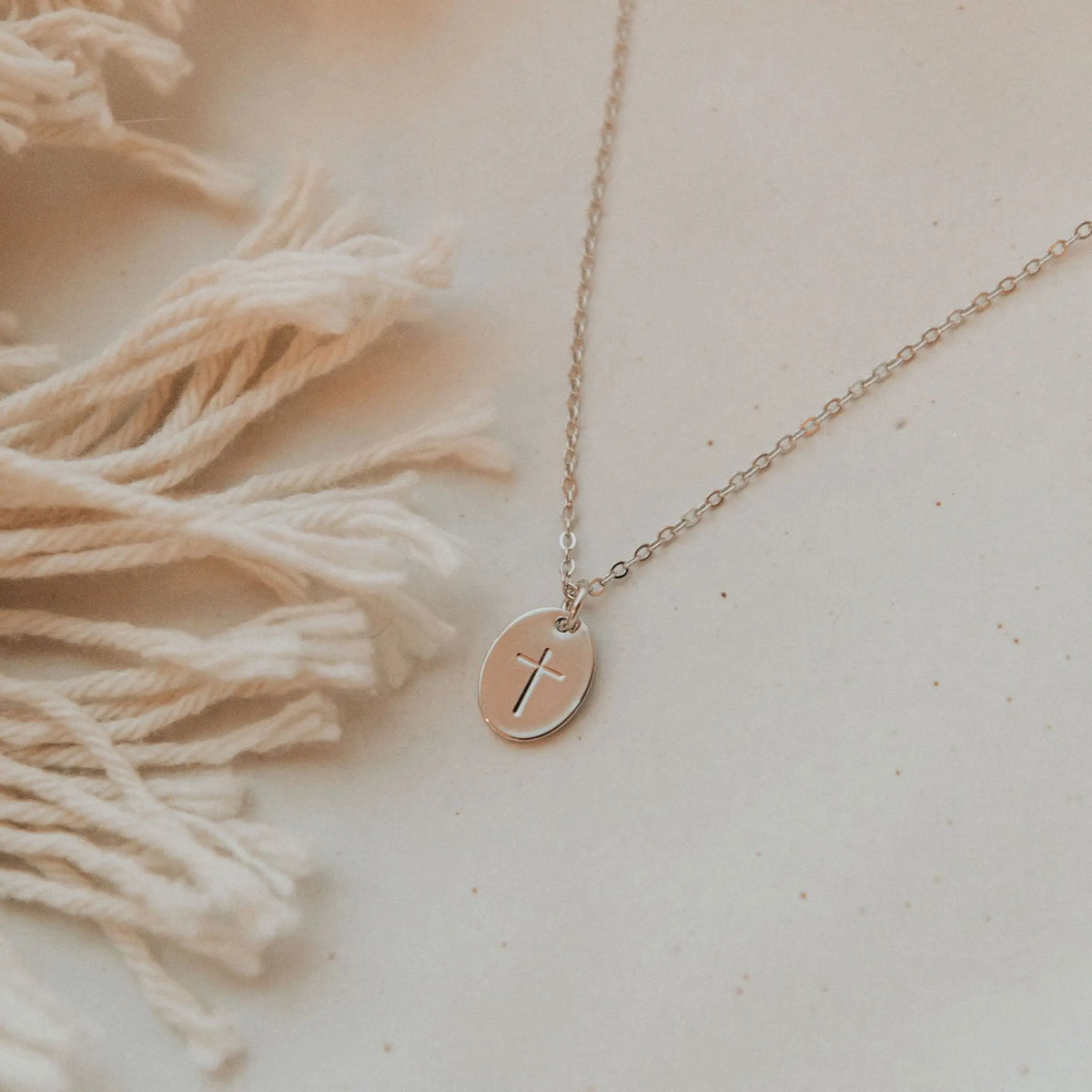 Gold necklace with a cross pendant on a textured beige surface