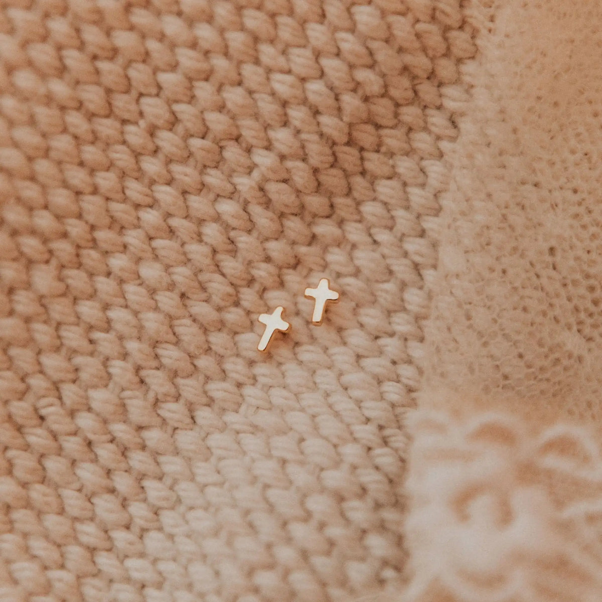 Small cross-shaped earrings on a textured beige fabric background