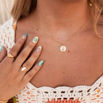 Close-up of a person wearing a gold necklace with a small pendant, hand with colorful nail polish, and rings.