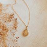 Gold necklace with a pendant on a light beige background with dried flowers.