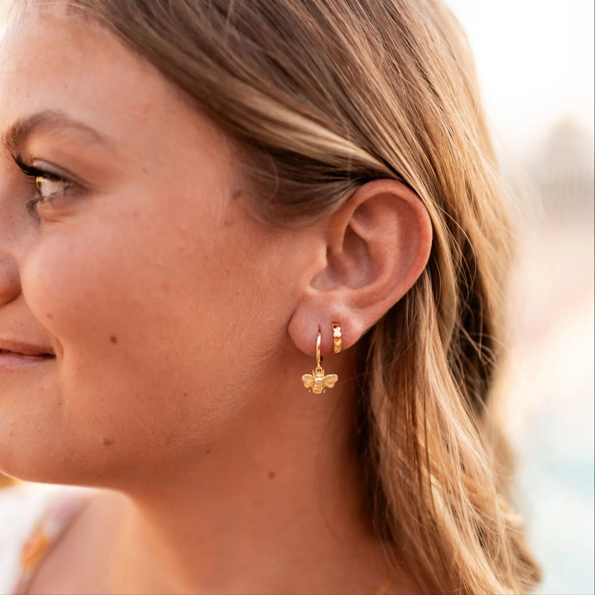 Close-up of a woman wearing gold bee-shaped earrings with a blurred background
