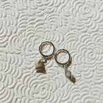 Two silver earings on a textured beige surface