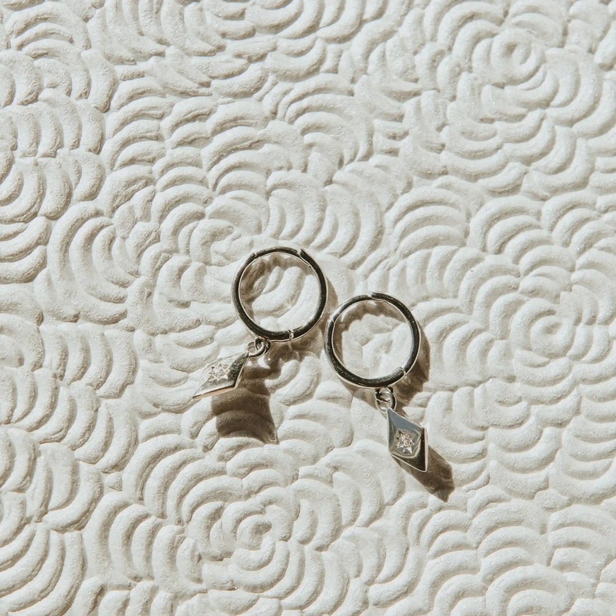 Two silver earings on a textured beige surface
