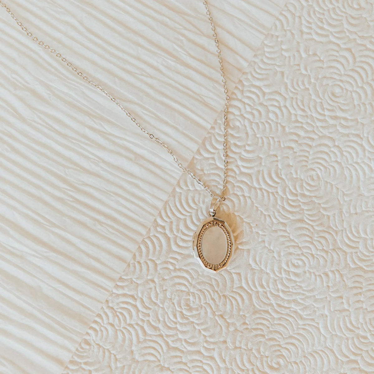 Gold necklace with a locket pendant on a textured beige surface